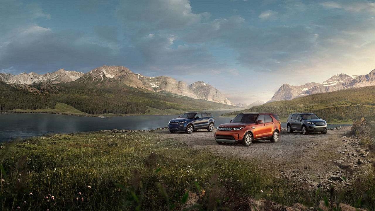 Land Rover vehicles parked near a lake mountains background