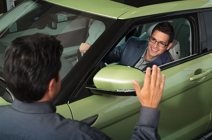 Person greets another one who driving a green land rover vehicle