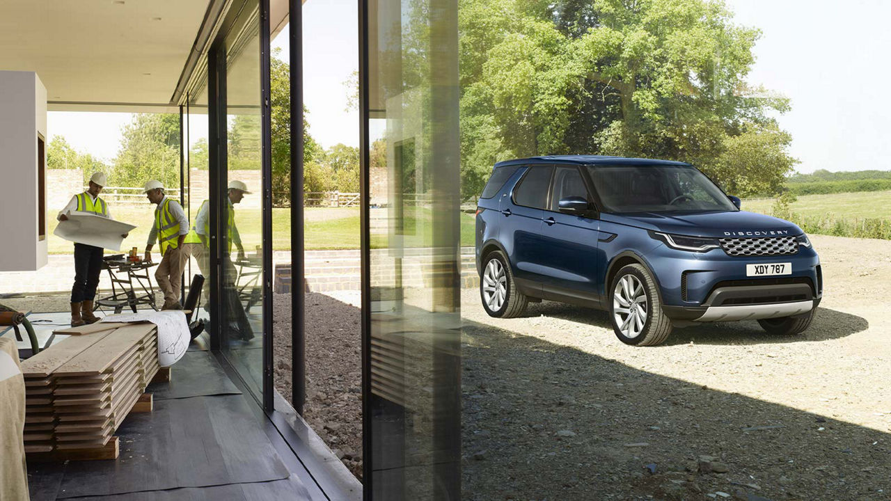 Land Rover Discovery in navy blue is parked next to a house being built by a group of experts