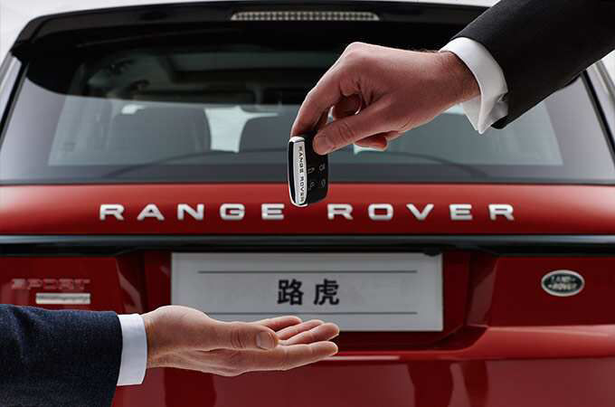 Handing a car key to someone in front of a range rover