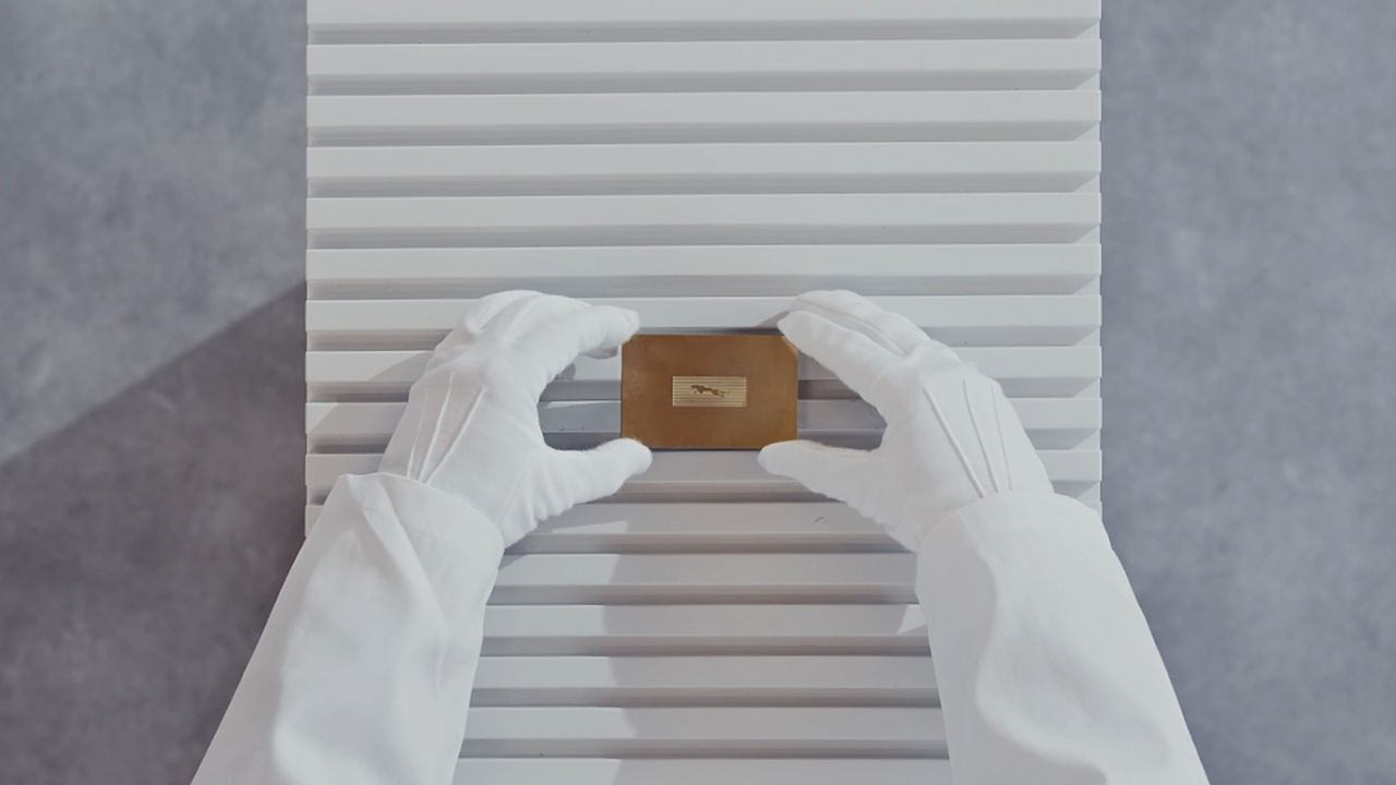 Gloved hands holding a small wooden block against a striped background.
