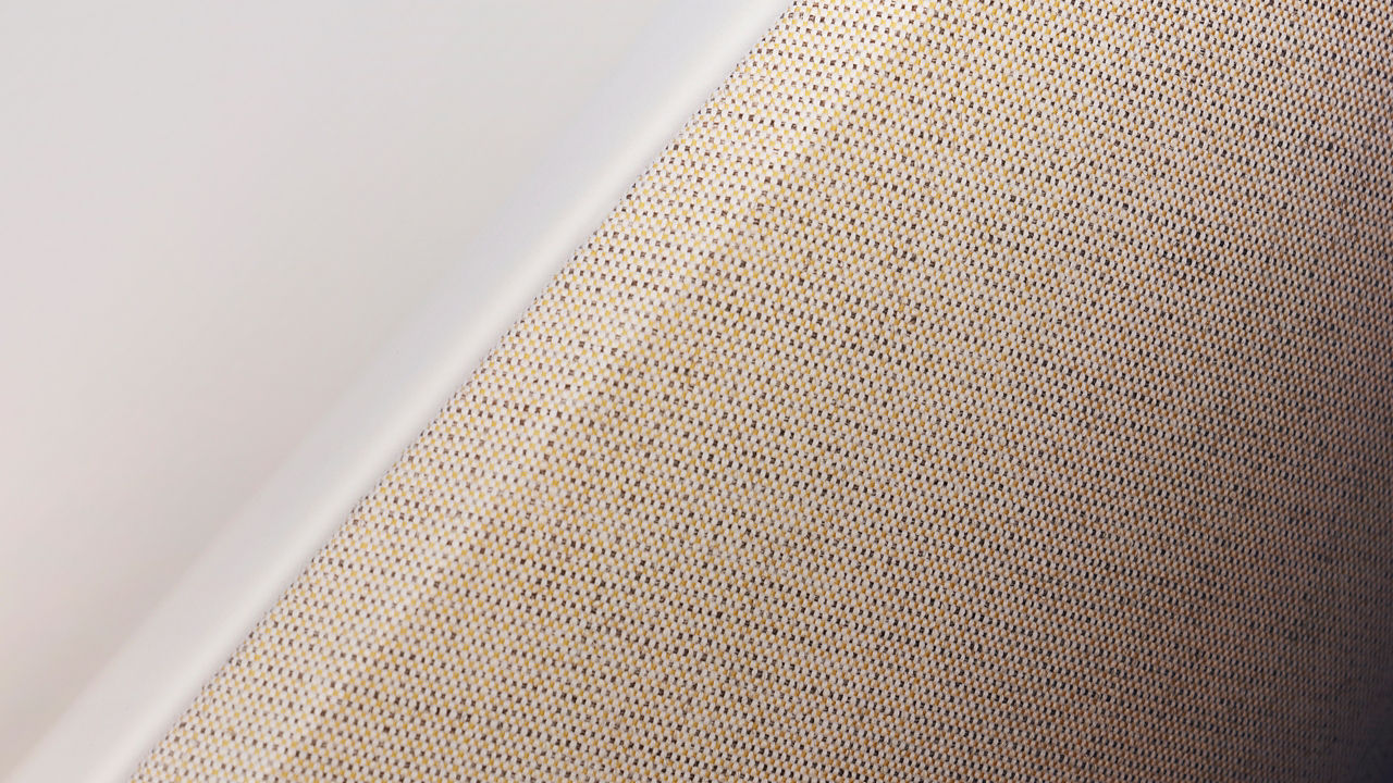 Close-up view of a beige woven textile fabric placed beside a smooth white surface.