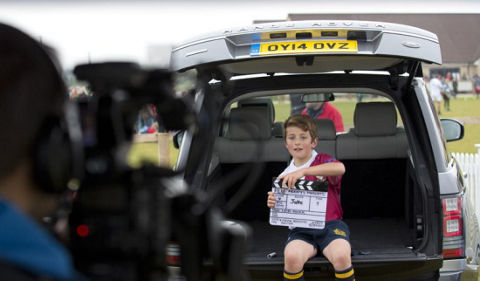 Child holding clapperboard sitting in the back of a Range Rover