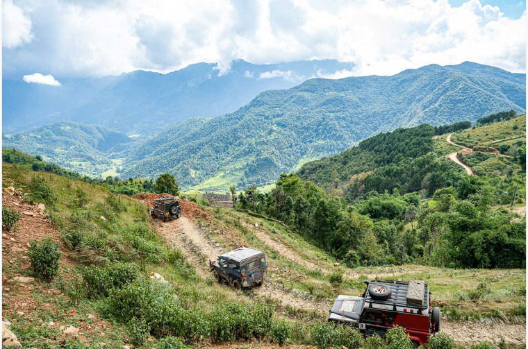 Land Rover vehicles driving on dirt road in mountain landscape